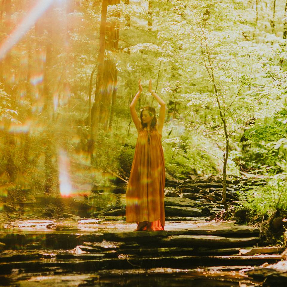 amanda standing in the woods, her hands up in the air above her head