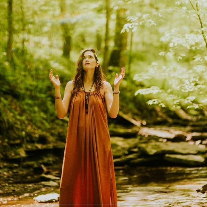 amanda standing in the woods with her hands bent at the elbows up towards the sky